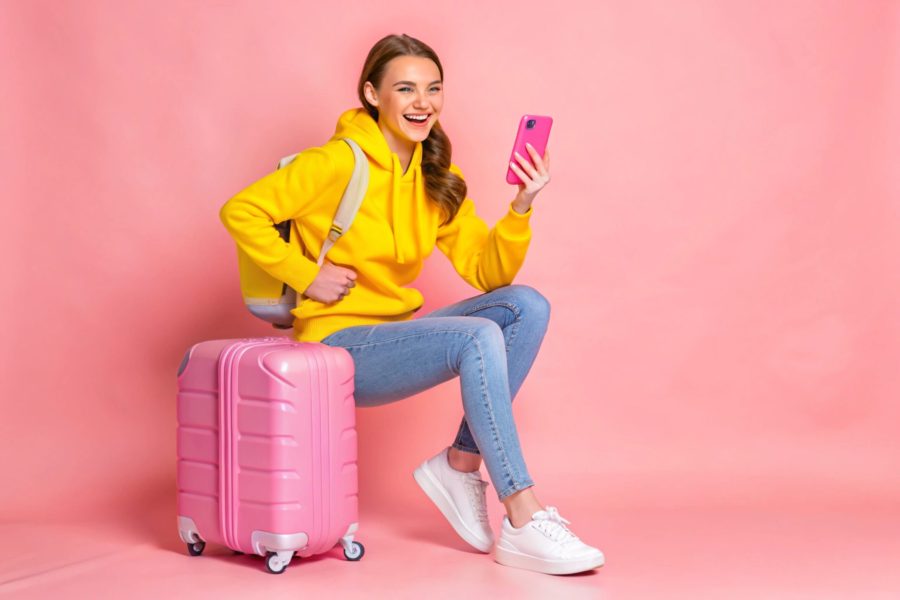 chica sentada sobre maleta rosa reservando lockers en su movil